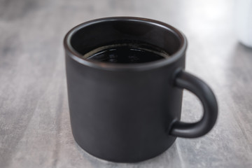 Closeup image of a black ceramics cup of hot coffee on table in modern cafe