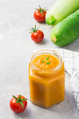 Vegetable marrow spread in a glass jar and ingredients on concrete background. Selective focus, space for text.