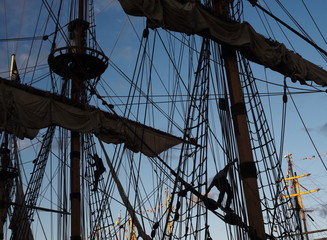 Tall ship masts and rigging silhouetted against a dramatic sky at sunset