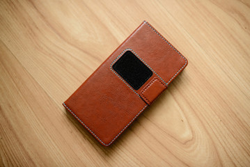 Brown leather case for mobile phone-on a wooden surface.
