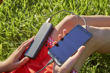 Powerbank connected with mobile phone in girl's hands outdoors
