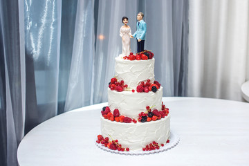 Wedding cake with figurines of the bride and groom on top decorated with strawberries on the tiers