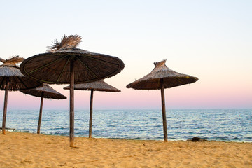 Sanset on sea with golden sand and straw-colored umbrellas.