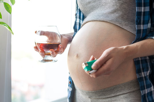 A pregnant woman with a belly holding a glass of whiskey and cigarette. Concept alcohol and bad habits during pregnancy