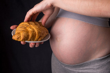 A pregnant woman with belly holding a plate of croissants. Concept weight control and an unhealthy diet during pregnancy
