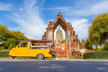 Young asian female traveler with backpack traveling sitting on taxi or Tuk Tuk and see map travel with old temple (Wat Mahathat) background, Ayutthaya Province, Thailand - obrazy, fototapety, plakaty