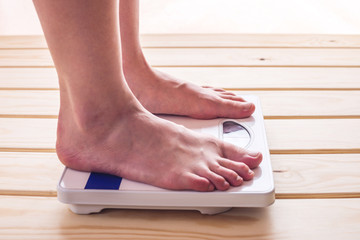 Female feet standing on mechanical scales for weight control on wooden background. Concept of...