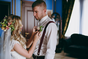 Bride dresses a flower boutonniere to the groom on the shirt