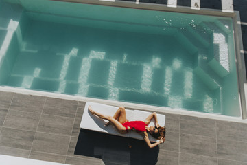 Young woman lying by the pool on sunbed