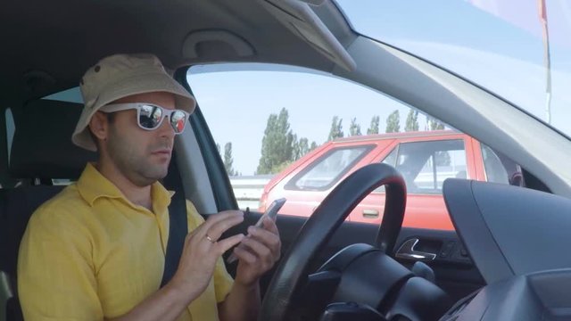 Man driving car on highway and texting on smartphone. Man with mobile telephone, driver with cell phone, driving car on street, using smartphone text messaging and internet. Danger and risk on road