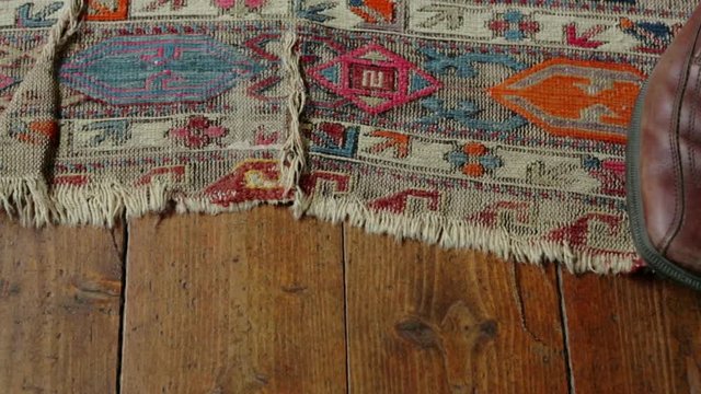 Old antique worn carpet on wooden floor. Camera travel ends on a pair of brown shoes.