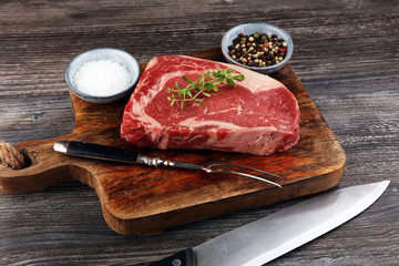 Raw fresh meat Ribeye Steak, seasoning and meat fork on dark background