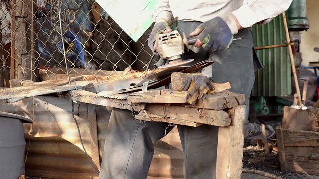 Close up a worker sharpening a traditional broad blade with an electric grinding in his workshop
