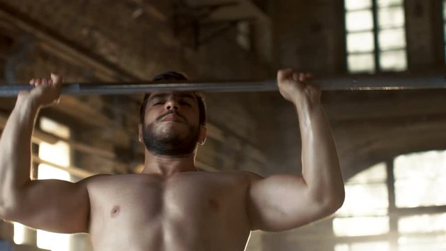 Close-up of a Muscular Shirtless Man Lifting Heavy Barbell and Doing Military Press Bodybuilding Exercise in the Industrial Gym Building. Shot on RED EPIC-W 8K Helium Cinema Camera.