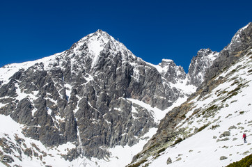 Climber approaching the climbing route. In the background is steep alpine peak with the observatory atop of it