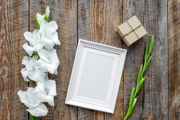 Blank photo frame near flower gladiolus on rustic wooden background top view mockup