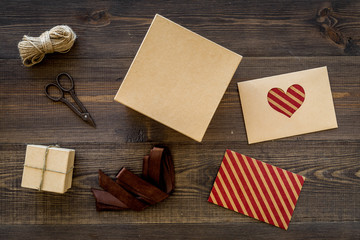 Fototapeta na wymiar To wrap gift. Box, kraft paper, envelope, greeting card, ribbon, sciccors on wooden background top view