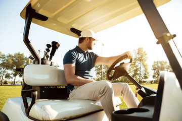 Male golfer driving a cart with golf clubs bag