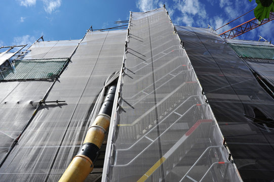 Teleskop-Bauschuttrutsche am Gerüst für die Renovierung der Fassade eines Verkaufsgebäudes mit Sicherheitsnetz