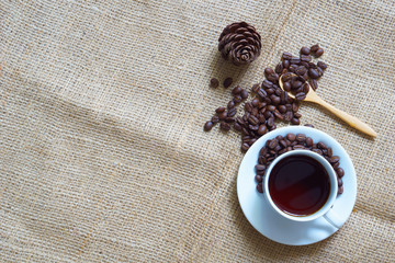 coffee concept. coffee in white cup with roasted coffee bean and wooden spoon and pine cones on sackcloth. copy space for your text