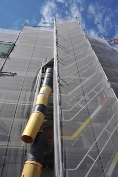 Teleskop-Bauschuttrutsche am Gerüst für die Renovierung der Fassade eines Verkaufsgebäudes mit Sicherheitsnetz