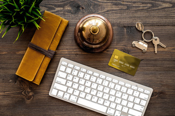Book hotel online. Bank card and purse near service bell and keyboard on dark wooden table background top view