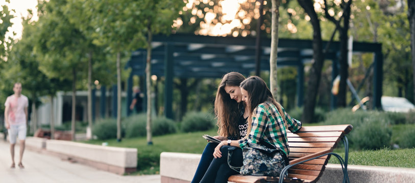 Teen girls back to school bargain.Showing the elementary school supplies list.Both are eagerly waiting to see the school supply results. Happily sitting on a wooden bench, legs crossed.Back to school