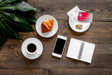 Restaurant bill and bank card near cup of coffee and bakery on dark wooden table top view