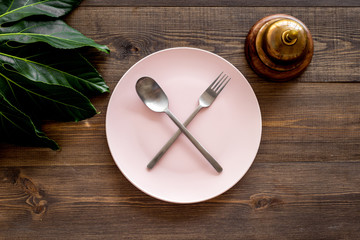 Ask for the bill at restaurant. Service bell near plate whith crossed spoon and fork on wooden table top view