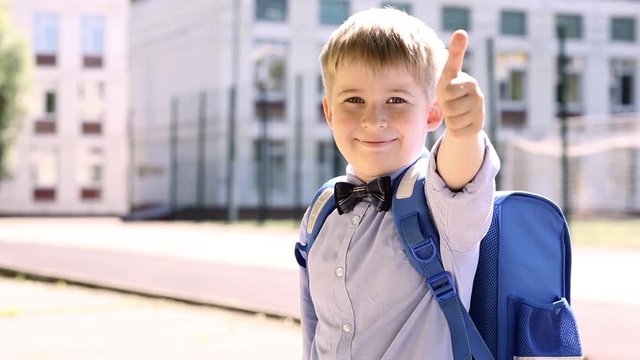  Smiling  boy  showing thumbs up sign. Funny child on the background of school.