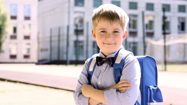 Funny schoolboy on the background of school. A child in school uniform with a knapsack.