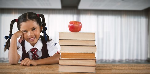 Composite image of schoolgirl leaning by books and apple on desk