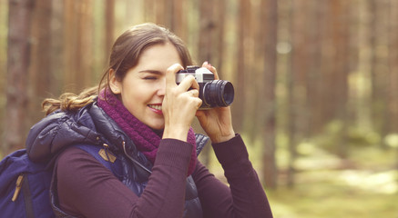 Young, beautiful and happy woman walking in forest and taking pictures. Camp, adventure, trip, hiking concept.