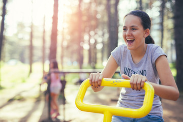 Fototapeta na wymiar Young smiling teenage girl does exercises at simulator in park