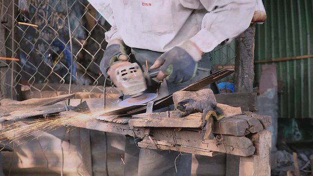 Close up a worker sharpening a traditional broad blade with an electric grinding in his workshop
