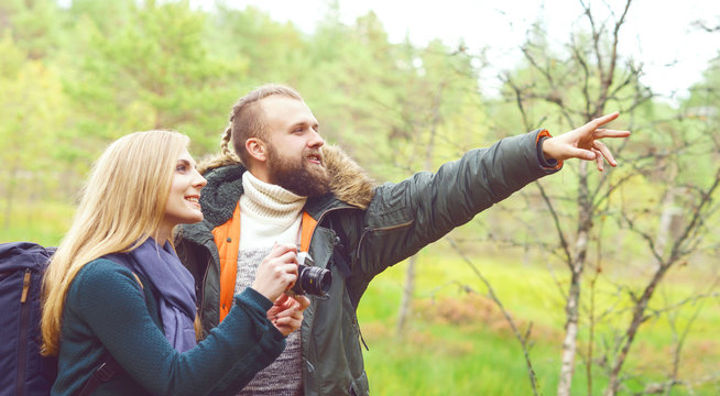 Young beautiful couple walking in forest and taking pictures. Camp, tourism, hiking concept.