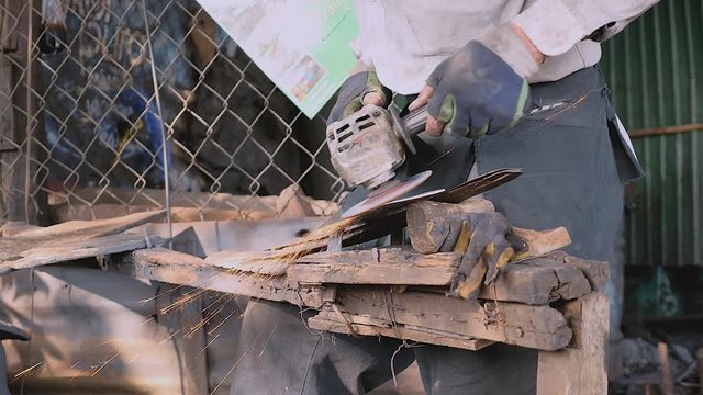Close up a worker sharpening a traditional broad blade with an electric grinding in his workshop