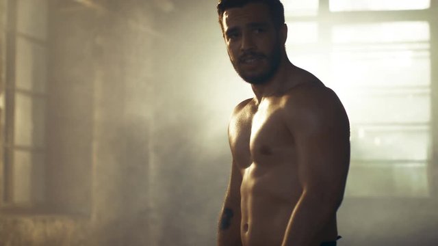 Handsome Shirtless Man with Naked Muscular Torso with Visible Six Pack Stands Resting after Bodybuilding Exercise. He's in the Middle of Abandoned Factory Building. 