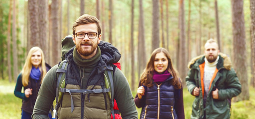 Young happy friends walking in forest and enjoying a good autumn day. Camp, tourism, hiking, trip, concept.