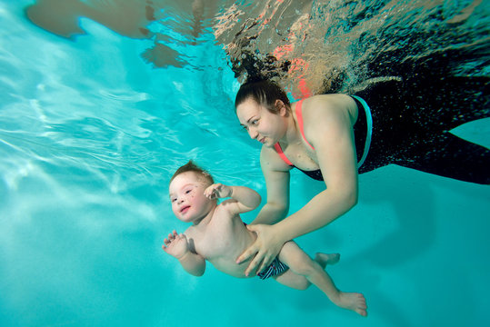 Instructor, mom teaches and helps the baby to swim underwater in the pool. Portrait. The view from under the water. Landscape orientation