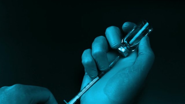 Syringe needle pierces the rubber stopper of the glass vial and filling syringe from glass ampule on black background