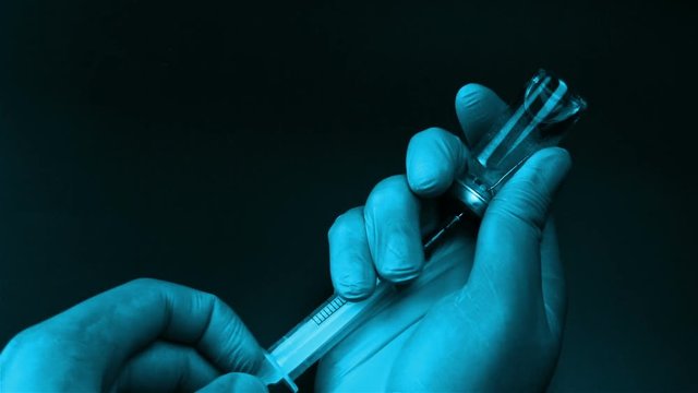 Syringe needle pierces the rubber stopper of the glass vial and filling syringe from glass ampule on black background
