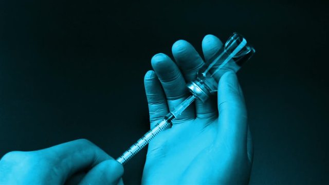 Syringe needle pierces the rubber stopper of the glass vial and filling syringe from glass ampule on black background
