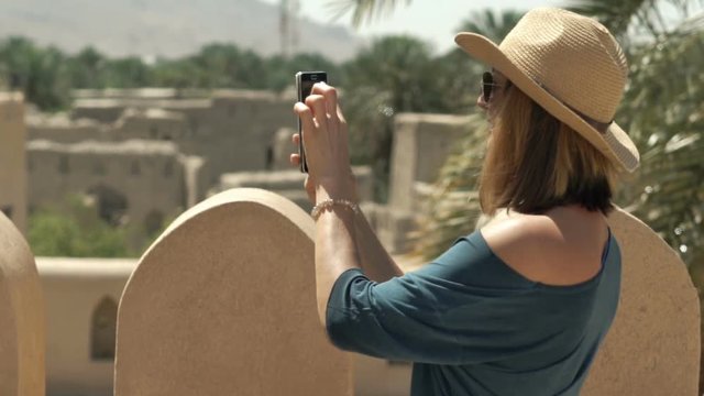 Woman taking photo with cellphone of ancient fort in Oman
