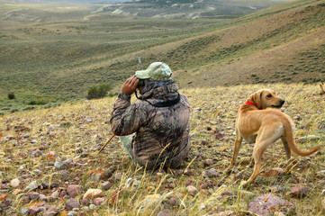Coyote hunter and dog scanning for prey from hill