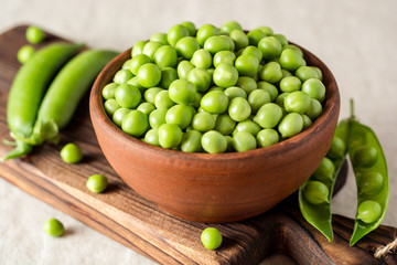 Fresh green peas in ceramic bowl on gray stone background