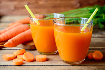 Fresh carrot juice in glasses on rustic wooden table.