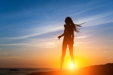 Silhouette of flexible dancing girl on the sea coast during a sunset.