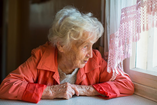 An elderly woman looks out the window of the house.