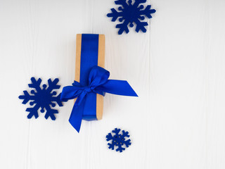 new Christmas gift with blue ribbon, bowknot, next blue snowflakes. On white wood background, copy space for text